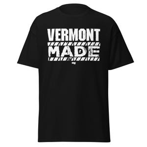 May include: Black t-shirt featuring the text "VERMONT MADE" in distressed white lettering. The text is arranged in two lines, with "VERMONT" above "MADE". The design includes horizontal lines above and below the word "MADE".