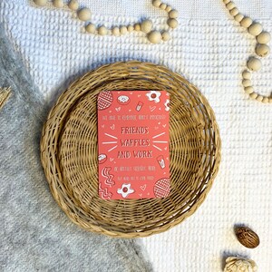May include: A pink card with a white border and a message that reads "We have to remember what's important! Friends, Waffles and Work or Waffles, Friends, Work but no one has to core them". The card is decorated with hearts, waffles, eggs, bacon, and donuts.