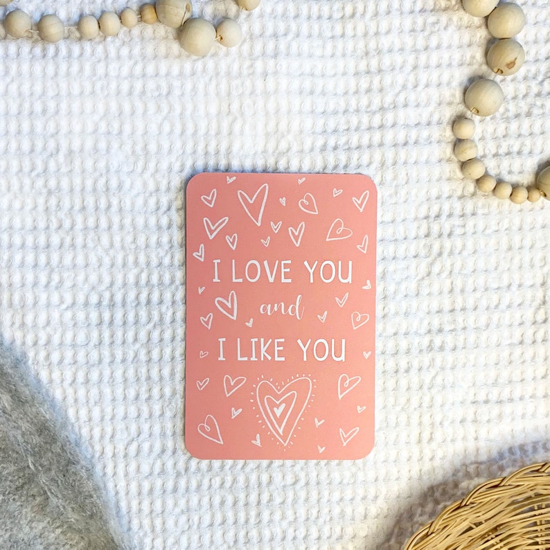 May include: Pink card with white hearts and the text "I love you and I like you" written in a handwritten style.