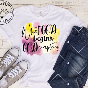 May include: White t-shirt with a watercolor design and the text "What God begins God completes".