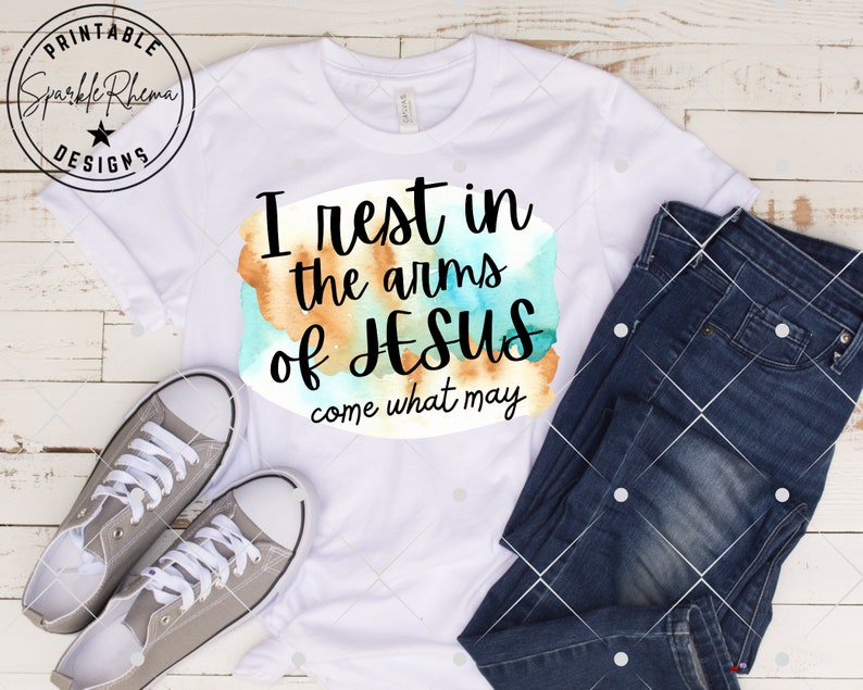 May include: White t-shirt with a watercolor design and the text "I rest in the arms of Jesus come what may".