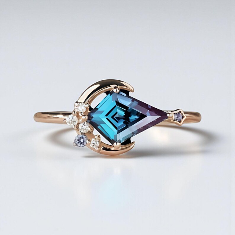 May include: A rose gold ring with a kite-shaped teal and purple gemstone. The ring features a crescent moon design with small white and blue accent stones, and a star-shaped stone on the band.