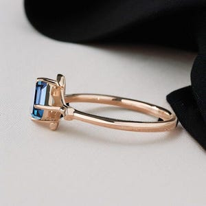 May include: A rose gold ring with a rectangular, deep blue gemstone. The ring has a slender, polished band and a delicate setting. The design is elegant and modern, suitable for everyday wear or special occasions. The ring's measurements are in centimetres.