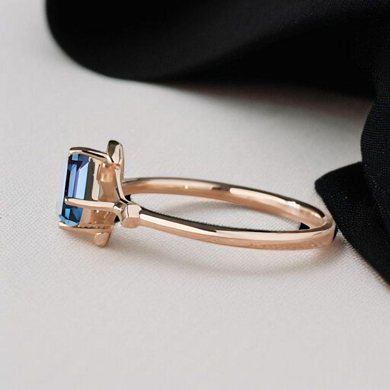 May include: A rose gold ring with a rectangular, deep blue gemstone. The ring has a slender, polished band and a delicate setting. The design is elegant and modern, suitable for everyday wear or special occasions. The ring's measurements are in centimetres.
