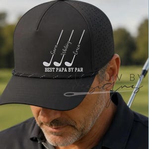 May include: Black golf cap with the text "BEST PAPA BY PAR" and the names "Sara", "Whitney", and "Erica" printed on it. The cap has a perforated side panel and a rope detail around the brim.