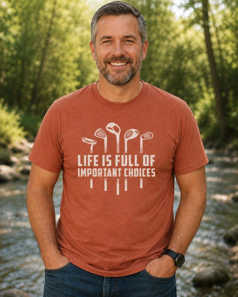 Puede incluir: Una camiseta de color &oacute;xido con el texto blanco "LIFE IS FULL OF IMPORTANT CHOICES", junto con gr&aacute;ficos de palos de golf. La camiseta la lleva una persona con barba gris y pelo oscuro.
