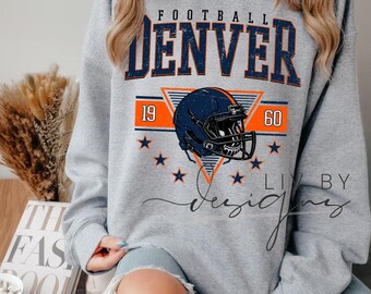 Puede incluir: Sudadera gris con la inscripción "FOOTBALL DENVER" en azul marino y naranja. El diseño incluye un casco de fútbol americano, los números "19" y "60" y gráficos de estrellas. También se ve el texto "LIV BY Designs".
