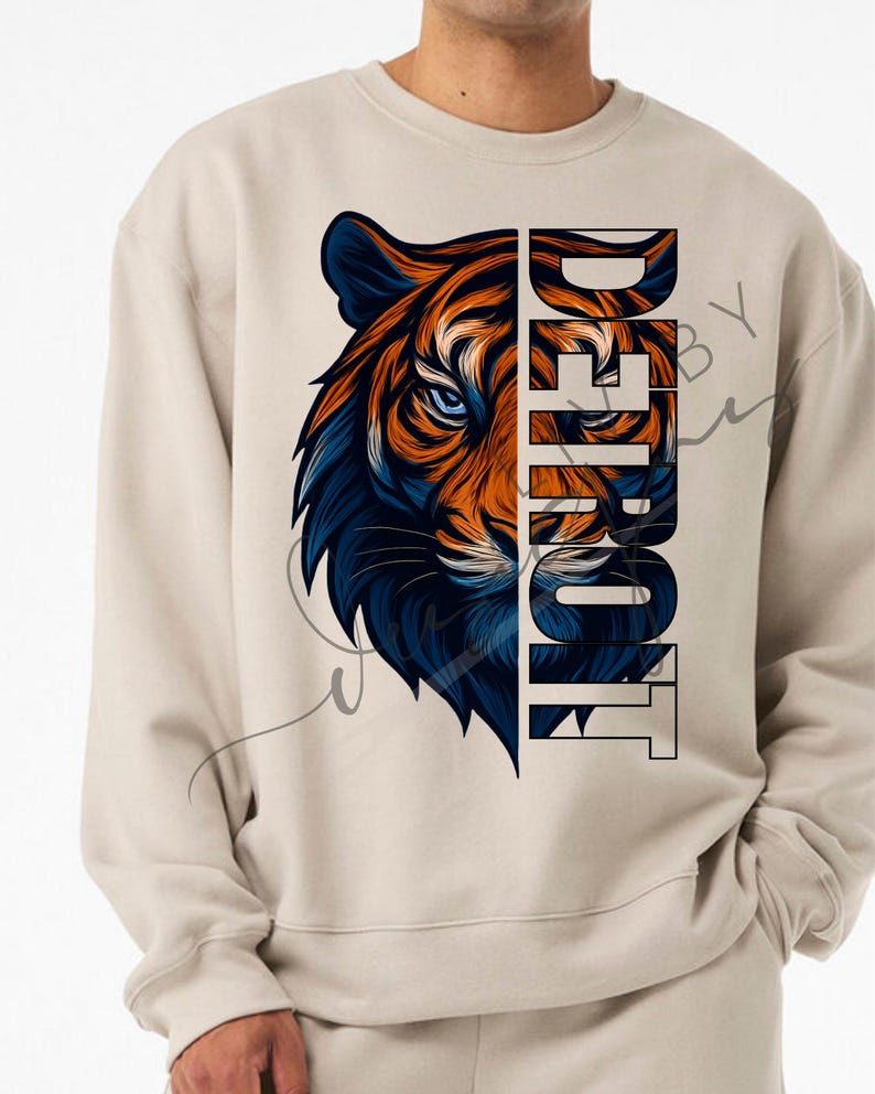May include: Beige sweatshirt with a tiger graphic in orange and blue. The word "DETROIT" is printed vertically in a bold font. The design is centered on the front of the sweatshirt, offering a striking visual.