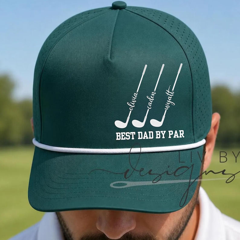 May include: Dark green golf cap with white text and accents. The cap features three golf club graphics with names above them and the phrase "BEST DAD BY PAR" below. A white rope detail accents the brim.