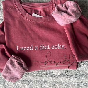 May include: A maroon sweatshirt with the text "I need a diet coke." embroidered on the front.
