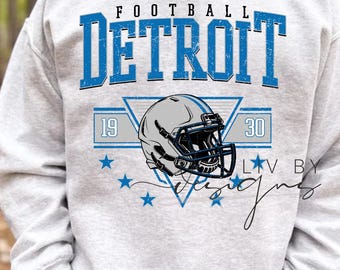 May include: A light gray sweatshirt with the word "FOOTBALL DETROIT" in blue block letters. Below the text is a football helmet graphic and the numbers "19" and "30". The sweatshirt also has blue star graphics.