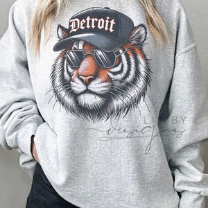 May include: Gray sweatshirt with a graphic of a tiger wearing sunglasses and a black baseball cap that says "Detroit".