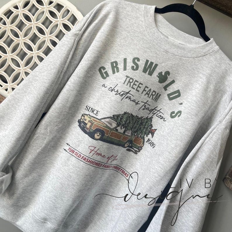 May include: A gray sweatshirt with a Christmas-themed graphic print. The print features a station wagon with a Christmas tree on top, the text "Griswold's Tree Farm", and the words "a Christmas tradition since 1989".