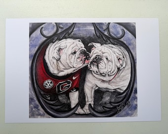 May include: A colored pencil drawing of two white bulldogs framed by a dark, ornate circular border. The left bulldog wears a red jersey with a white G logo and SEC emblem. The background features a textured blue and black wash effect.
