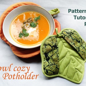 Può includere: Un sottopentola a forma di foglia verde con una fodera in tessuto marmoreo nero e verde. Il sottopentola è su una superficie bianca accanto a una ciotola di zuppa arancione con un cucchiaio di panna e semi di zucca.