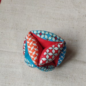 May include: A colorful fabric ball with a geometric pattern in shades of blue, red, and orange. The ball is made of multiple fabric pieces sewn together.