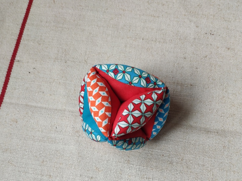 May include: A colorful fabric ball with a geometric pattern in shades of blue, red, and orange. The ball is made of multiple fabric pieces sewn together.