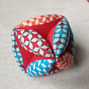 May include: A red, blue, and orange fabric cube with a geometric pattern. The cube is made of multiple fabric panels sewn together.