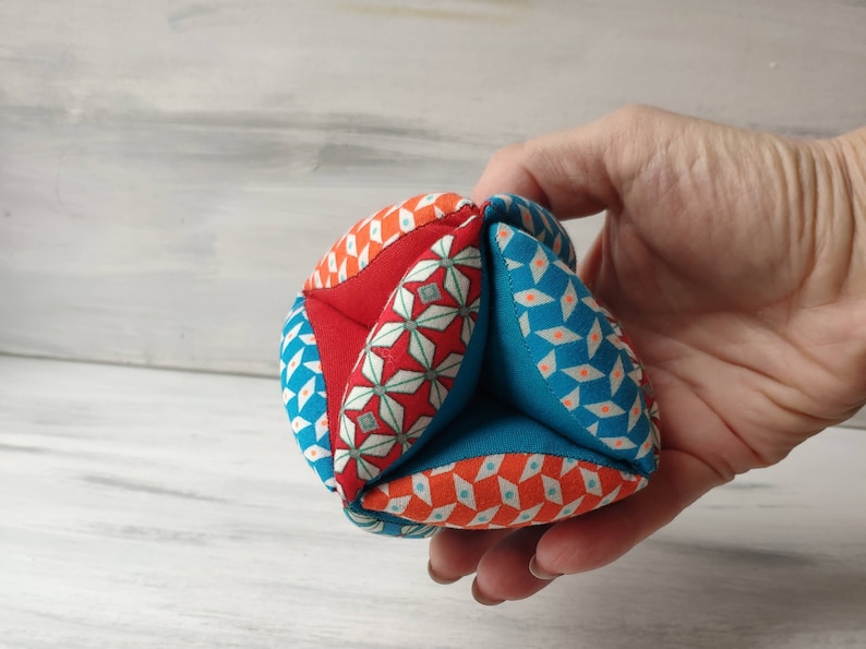 May include: A colorful fabric ball with a geometric pattern in shades of red, blue, and orange. The ball is made of multiple fabric panels sewn together.