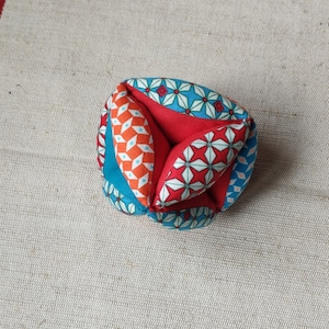 May include: A colorful fabric ball with a geometric pattern in shades of red, blue, and white. The ball is made of multiple fabric pieces sewn together.