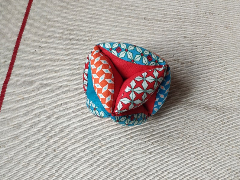 May include: A colorful fabric ball with a geometric pattern in shades of red, blue, and white. The ball is made of multiple fabric pieces sewn together.