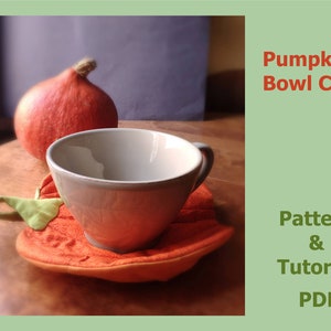 以下が含まれることがあります： オレンジ色の生地でできた、かぼちゃの形をしたボウル用コージー。緑の葉っぱのディテールが施されています。コージーは白いセラミックボウルを持っています。画像には「Pumpkin Bowl Cozy Pattern & Tutorial PDF」というテキストが含まれています。