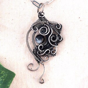 May include: A handcrafted silver wire pendant necklace. The pendant features intricate wire wrapping with a central black and white stone. The necklace has a delicate chain and a unique, artistic design, perfect for adding a touch of elegance to any outfit.
