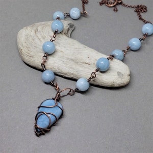 May include: A handmade necklace with pale blue gemstone beads and a wire-wrapped pendant. The necklace has copper-coloured chain and wire detailing. The pendant is a light blue, teardrop-shaped stone.