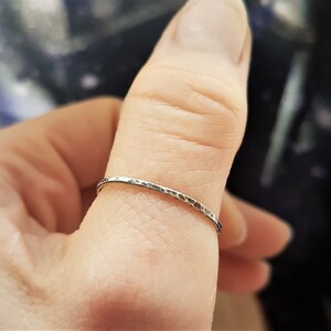 May include: A thin, hammered silver ring. The ring has a textured surface and a simple, minimalist design. The ring is worn on a finger, showcasing its delicate and understated elegance. This piece is suitable for everyday wear.