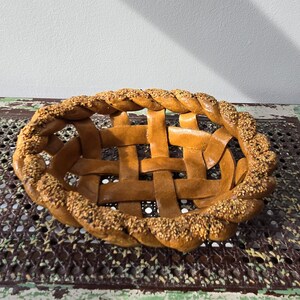 May include: A woven bread bowl with a brown, braided rim and a lattice pattern. The bowl is covered in sesame seeds.