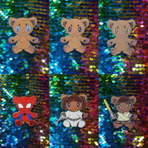 Puede incluir: Colección de pines de esmalte con personajes de osos de dibujos animados. Los pines incluyen osos con ojos azules, rosas y verdes, y osos disfrazados de Spider-Man, Princesa Leia y un Jedi. Sobre un fondo de lentejuelas.