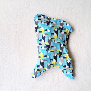 May include: A blue fabric with a pattern of toucans in black, yellow, and white. The fabric is shaped like a hood with a pointed top and two flaps on the sides.