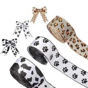 May include: Three rolls of ribbon with different patterns. One roll has a black and white paw print design, one has a black and white cow print design, and one has a brown and tan leopard print design. There are also three matching bows in the image.