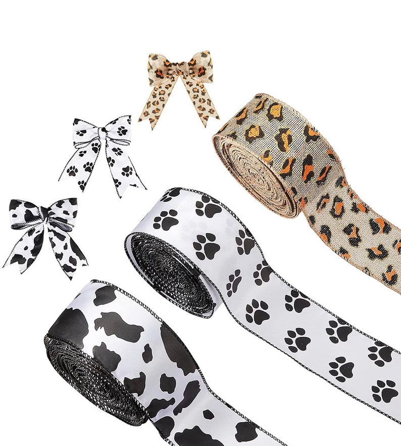 May include: Three rolls of ribbon with different patterns. One roll has a black and white paw print design, one has a black and white cow print design, and one has a brown and tan leopard print design. There are also three matching bows in the image.