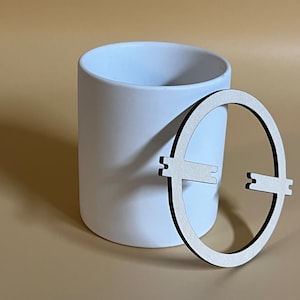 Może przedstawiać: Biała ceramiczna doniczka z drewnianym wycięciem w kształcie koła z czarnym obramowaniem. Wycięcie ma kształt koła z dwoma przecinającymi się liniami.