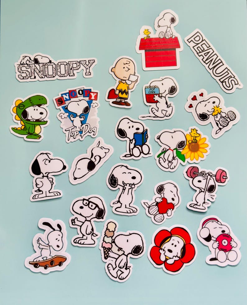 May include: A selection of Snoopy stickers in different poses and scenes. The stickers depict Snoopy with Charlie Brown, in a dinosaur costume, on a skateboard, and other designs. The words "Snoopy" and "Peanuts" are also visible.