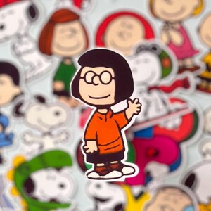 May include: A sticker of a cartoon character with black hair, glasses, and an orange top waving. Other cartoon character stickers surround it, set against a light blue background.