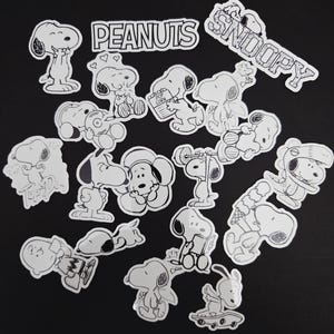 May include: A selection of black and white Snoopy stickers in different poses, including Snoopy with the words "Snoopy" and "Peanuts". The stickers show Snoopy holding popcorn, ice cream, and other items. The stickers are on a black background.