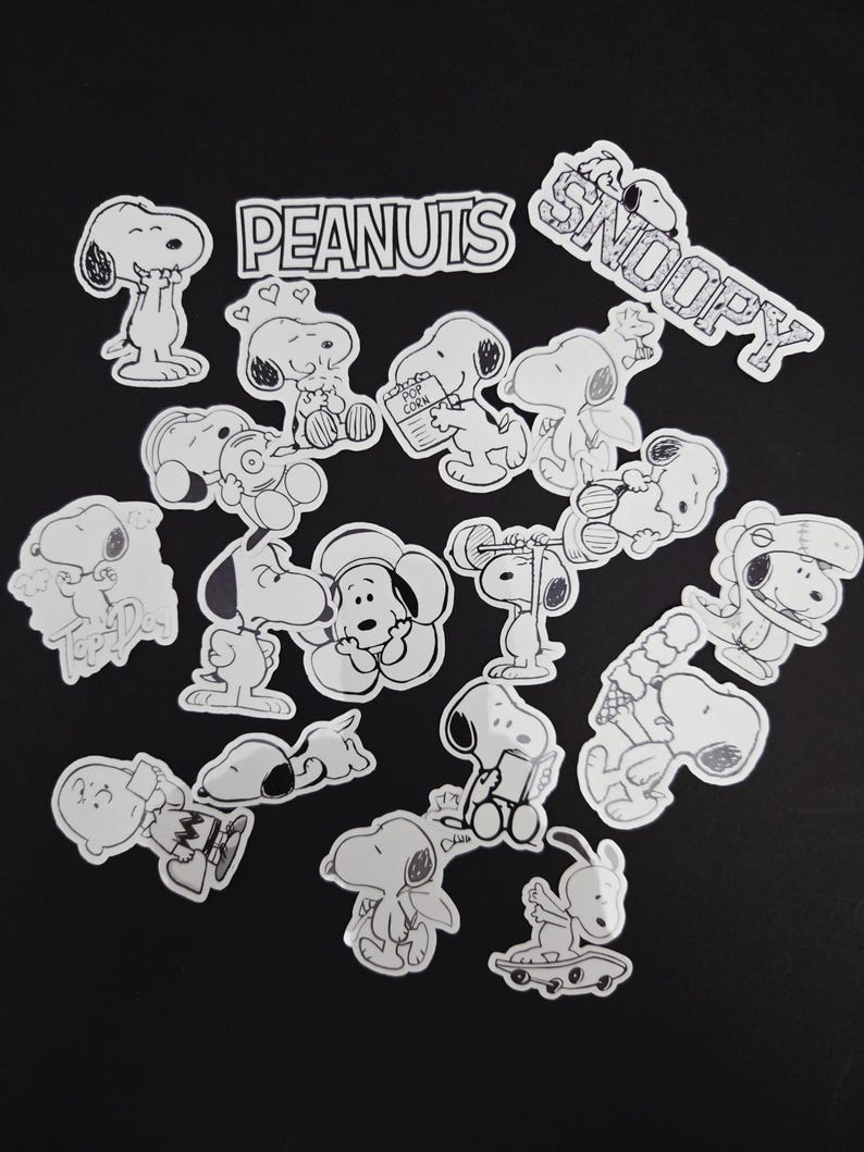 May include: A selection of black and white Snoopy stickers in different poses, including Snoopy with the words "Snoopy" and "Peanuts". The stickers show Snoopy holding popcorn, ice cream, and other items. The stickers are on a black background.