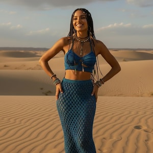 Puede incluir: Conjunto de top y falda de crochet azul. El top tiene cuello halter y detalles recortados. La falda es un diseño ajustado y largo. La modelo lleva varias pulseras y collares. El fondo es un paisaje desértico.