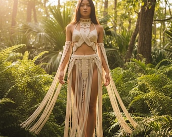 Puede incluir: Un conjunto de dos piezas de macramé en color crema que presenta un top estilo halter con detalles entrecruzados y una falda a juego con una cintura tejida intrincada y largos flecos fluidos que llegan hasta el suelo, incluyendo brazaletes.