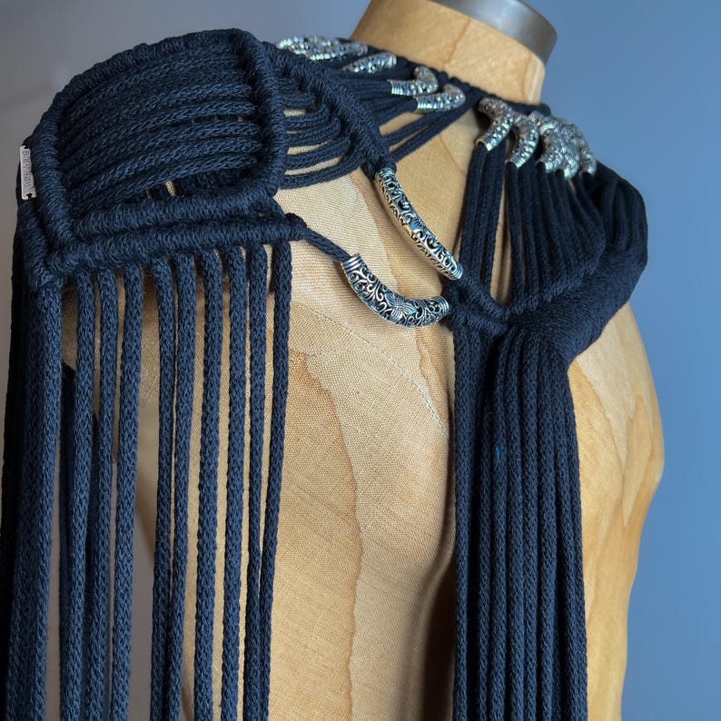 Peut inclure: Pi&egrave;ce d'&eacute;paule en macram&eacute; noir avec des accents en m&eacute;tal argent&eacute;. La pi&egrave;ce est faite d'un cordon noir &eacute;pais et pr&eacute;sente un d&eacute;tail de frange.