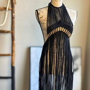 K&ouml;nnte beinhalten: Ein schwarzes Halstuch mit goldenen Akzenten und Fransen. Das Oberteil ist aus Makramee gefertigt und hat einen Boho-Stil.