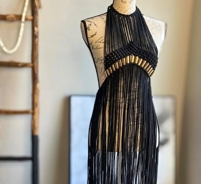 K&ouml;nnte beinhalten: Ein schwarzes Halstuch mit goldenen Akzenten und Fransen. Das Oberteil ist aus Makramee gefertigt und hat einen Boho-Stil.