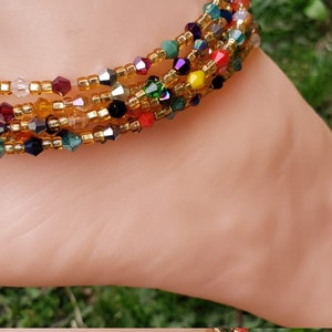 Pode incluir: Um tornozelo de contas multicoloridas com contas douradas e uma variedade de contas de vidro coloridas. O tornozelo é usado no tornozelo de uma pessoa.