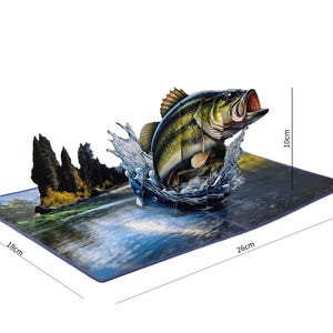 以下が含まれることがあります： 水から飛び出すラージマウスバスを描いた3Dポップアップカード。カードの高さは10cm、長さは26cm、幅は18cmです。魚は緑と黒の縞模様です。背景には川の風景が描かれています。