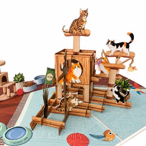 Puede incluir: Una tarjeta pop-up tridimensional que presenta una estructura de árbol para gatos de madera con múltiples niveles, plataformas y recortes. Varios gatos ilustrados en diversas poses están colocados sobre la estructura, junto a cuencos de comida.