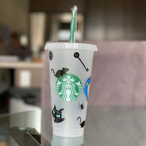 Pode incluir: Copo Starbucks de pl&aacute;stico transparente com canudo verde. O copo &eacute; decorado com adesivos de gato preto, aranha e rato, juntamente com o logotipo verde da Starbucks. Uma chave e um bot&atilde;o tamb&eacute;m s&atilde;o vis&iacute;veis.