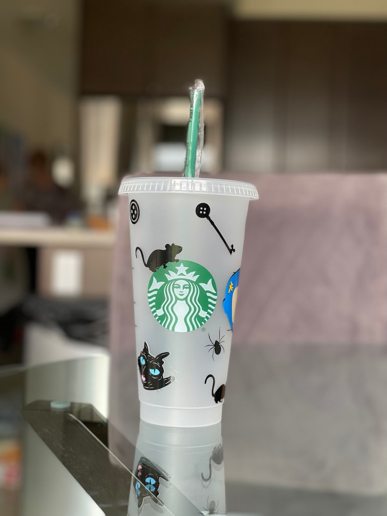 Pode incluir: Copo Starbucks de pl&aacute;stico transparente com canudo verde. O copo &eacute; decorado com adesivos de gato preto, aranha e rato, juntamente com o logotipo verde da Starbucks. Uma chave e um bot&atilde;o tamb&eacute;m s&atilde;o vis&iacute;veis.