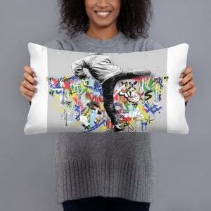 May include: A white pillow with a colorful graffiti design featuring a black and white figure kicking a wall. The figure is wearing a jacket and jeans.